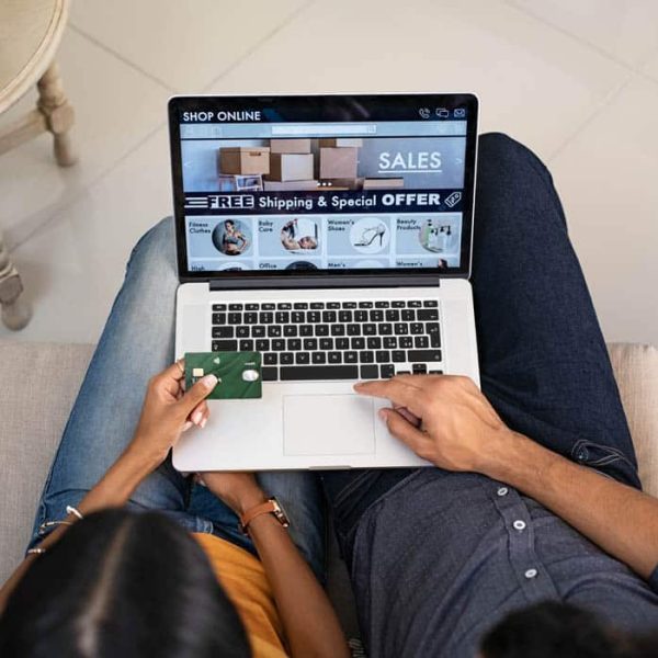 Top view of indian couple doing shopping online on website with laptop at home. High angle view of man and woman using laptop on legs and paying with credit card. Indian casual couple selecting product on ecommerce portal on computer.